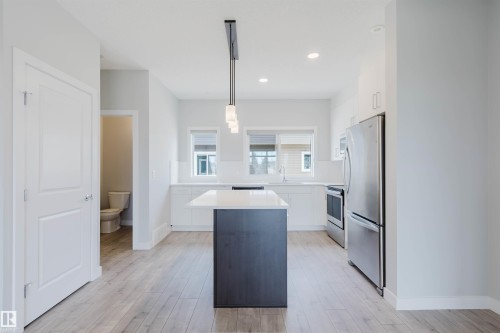 Kitchen featuring a dark-toned island with a white countertop, stainless steel appliances, white cabinetry, and wood-finish flooring - 3 11373 12 Avenue, Edmonton, AB - Indoor Photo Showing Kitchen