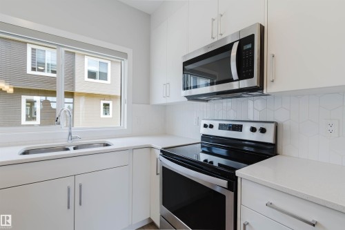 Modern kitchen featuring white cabinetry, light countertops, a stainless steel electric range, an over-the-range microwave, and a hexagonal tile backsplash - 3 11373 12 Avenue, Edmonton, AB - Indoor Photo Showing Kitchen With Double Sink