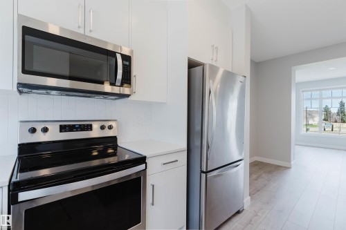 Kitchen showcasing stainless steel appliances, including an over-range microwave, electric range, and refrigerator - 3 11373 12 Avenue, Edmonton, AB - Indoor Photo Showing Kitchen With Stainless Steel Kitchen
