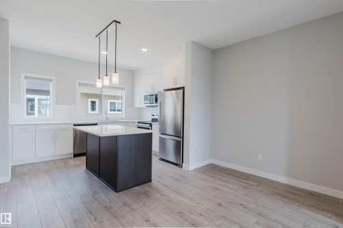 Modern kitchen featuring a dark-toned island with white countertop, white cabinetry, and stainless steel appliances - 3 11373 12 Avenue, Edmonton, AB - Indoor Photo Showing Kitchen With Stainless Steel Kitchen With Upgraded Kitchen
