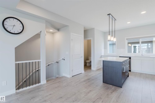 Light wood-finish flooring extending into the kitchen area with a dark gray island featuring a white countertop and pendant lighting - 3 11373 12 Avenue, Edmonton, AB - Indoor
