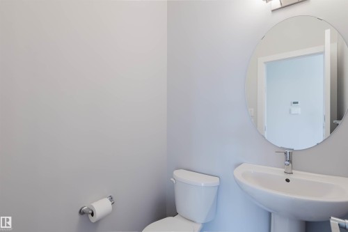 Pedestal sink with chrome faucet, complemented by a round wall-mounted mirror - 3 11373 12 Avenue, Edmonton, AB - Indoor Photo Showing Bathroom