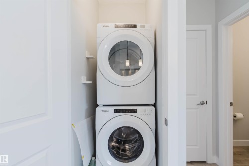 Stackable laundry appliances within a dedicated alcove, featuring white panel doors and light-toned walls - 3 11373 12 Avenue, Edmonton, AB - Indoor Photo Showing Laundry Room