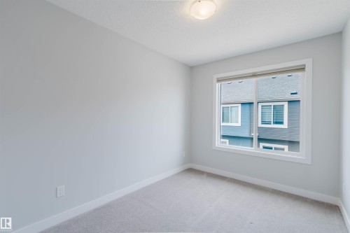Neutral-toned room featuring a large window, light gray carpeting, white baseboards, and a flush-mount ceiling light fixture - 3 11373 12 Avenue, Edmonton, AB - Indoor Photo Showing Other Room