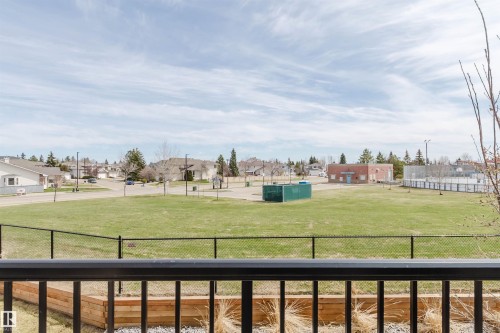 Expansive green space featuring a fenced sports court, adjacent brick building, and surrounding residential street with detached homes - 3 11373 12 Avenue, Edmonton, AB - Outdoor With Balcony