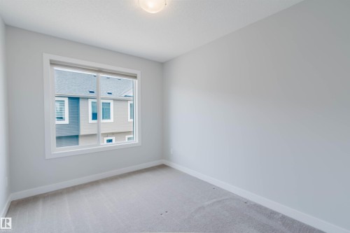 Bright room featuring a large window, neutral gray walls, light-colored carpeting, white trim, and a ceiling-mounted light fixture - 3 11373 12 Avenue, Edmonton, AB - Indoor Photo Showing Other Room