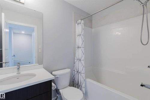 Full bathroom featuring a single vanity with a white countertop and dark wood-finish cabinetry, a built-in bathtub with shower, and white wall tile surround - 3 11373 12 Avenue, Edmonton, AB - Indoor Photo Showing Bathroom