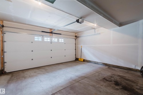 Spacious garage featuring a white sectional garage door with integrated windows, concrete flooring, and an automatic garage door opener - 3 11373 12 Avenue, Edmonton, AB - Indoor Photo Showing Garage