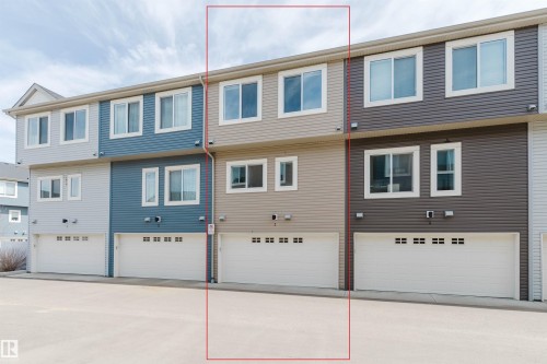 Multi-level townhome exterior featuring beige horizontal siding, white trim, and a white garage door - 3 11373 12 Avenue, Edmonton, AB - Outdoor