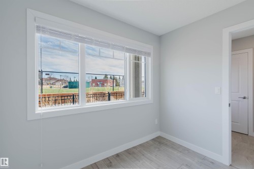 Bright room featuring a large window with white blinds, light gray walls, and wood-finish flooring - 3 11373 12 Avenue, Edmonton, AB - Indoor Photo Showing Other Room