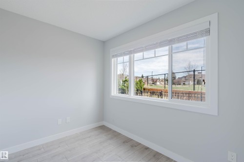 Bright interior space featuring a large picture window, light wood-finish flooring, white baseboards, and neutral wall paint - 3 11373 12 Avenue, Edmonton, AB - Indoor Photo Showing Other Room