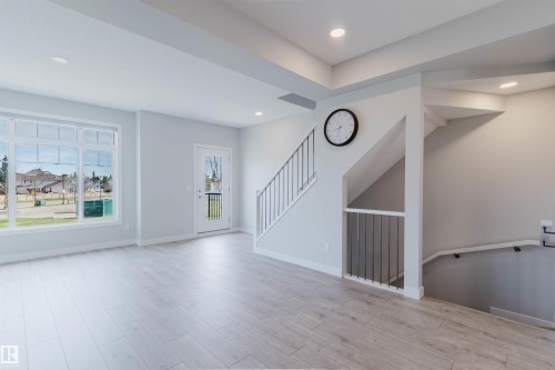 Open concept living space featuring light wood-finish flooring, recessed lighting, expansive windows, a glass-paneled exterior door, and a staircase with metal railings - 3 11373 12 Avenue, Edmonton, AB - Indoor Photo Showing Other Room