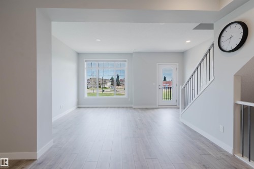 Bright living area featuring wood-finish flooring, a large multi-pane window, and a glass-paneled exterior door - 3 11373 12 Avenue, Edmonton, AB - Indoor