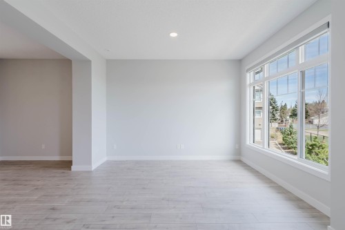 Spacious room featuring light wood-finish flooring, recessed ceiling lighting, and a large multi-pane window with roller shades - 3 11373 12 Avenue, Edmonton, AB - Indoor Photo Showing Other Room