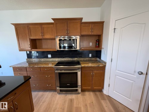 Kitchen featuring extensive cabinetry, stainless steel appliances, a tile backsplash, wood-finish flooring, and a pantry with built-in shelving - 2335 Rutherford Way, Edmonton, AB - Indoor Photo Showing Kitchen
