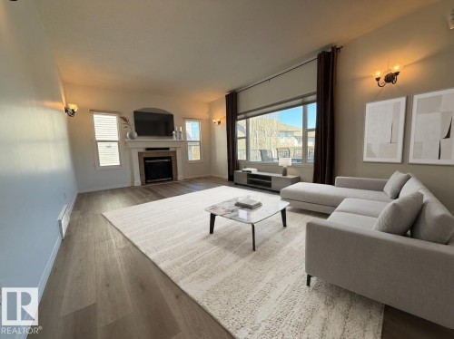 Spacious living area featuring wood-finish flooring, a contemporary fireplace with a white mantel, and two recessed windows - 2335 Rutherford Way, Edmonton, AB - Indoor Photo Showing Living Room With Fireplace