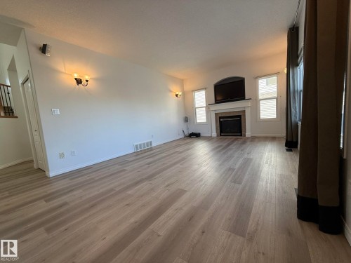 Spacious room featuring wood-finish flooring, a large window with white trim, and a decorative chandelier - 2335 Rutherford Way, Edmonton, AB - Indoor Photo Showing Other Room