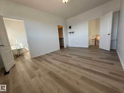 Spacious room featuring wood-finish flooring, white baseboards, and bright white walls - 2335 Rutherford Way, Edmonton, AB - Indoor Photo Showing Other Room
