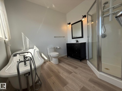 Freestanding clawfoot bathtub with a chrome faucet, black vanity with a white countertop and rectangular sink, shower enclosure with a glass door, light wood-finish flooring, and bright white walls - 2335 Rutherford Way, Edmonton, AB - Indoor Photo Showing Bathroom