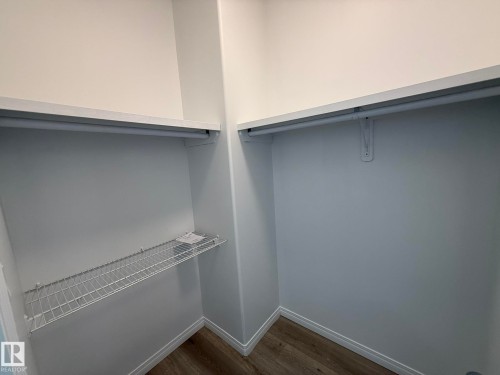 Walk-in closet featuring wood-finish flooring, white baseboards, white walls, and built-in shelving and hanging rods - 2335 Rutherford Way, Edmonton, AB - Indoor With Storage
