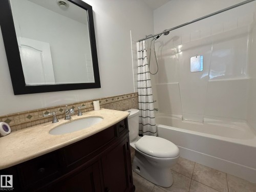 Bathroom featuring a dark wood-finish vanity with an undermount sink, a light-toned countertop, and a tiled backsplash - 2335 Rutherford Way, Edmonton, AB - Indoor Photo Showing Bathroom