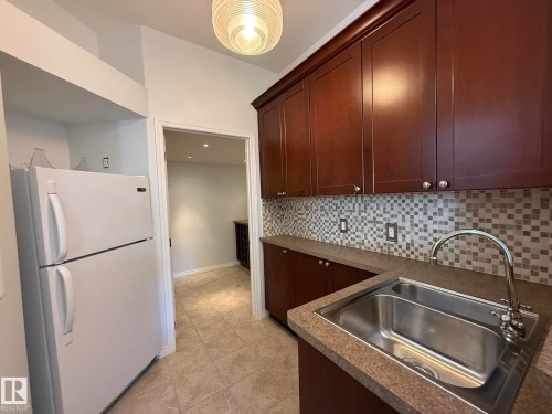Kitchenette with dark wood cabinetry, a mosaic tile backsplash, and a double basin stainless steel sink with a gooseneck faucet - 2335 Rutherford Way, Edmonton, AB - Indoor Photo Showing Kitchen