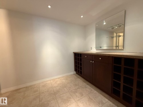 Custom built-in cabinetry featuring integrated wine storage, a solid surface countertop, and a large wall-mounted mirror with glass shelving - 2335 Rutherford Way, Edmonton, AB - Indoor Photo Showing Other Room