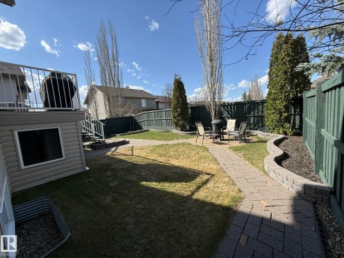 Expansive backyard featuring a paver patio with a fire pit, bordered by a decorative block retaining wall and mature evergreen trees - 2335 Rutherford Way, Edmonton, AB - Outdoor
