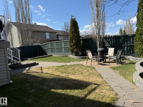 Expansive backyard featuring a paver patio with a fire pit, mature trees, a privacy fence, and concrete block retaining walls - 2335 Rutherford Way, Edmonton, AB - Outdoor