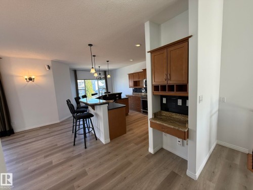 Open-concept kitchen and living area featuring wood-finish flooring, a kitchen island with seating, pendant lighting, and a built-in dry bar with granite countertop and cabinetry - 2335 Rutherford Way, Edmonton, AB - Indoor