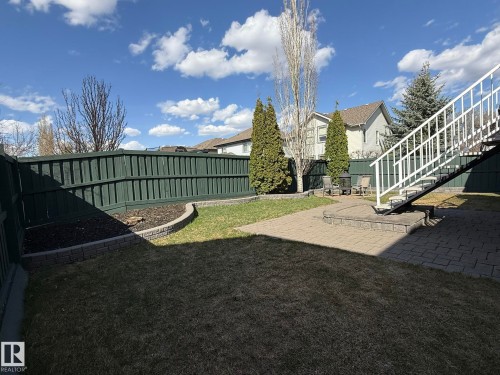 Expansive backyard featuring a dark green privacy fence, mature evergreen trees, and a paved patio area - 2335 Rutherford Way, Edmonton, AB - Outdoor