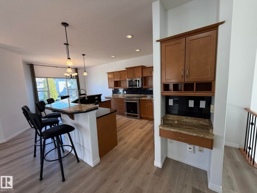 Kitchen featuring an eat-at island with a granite countertop, wood-finish flooring, stainless steel appliances, dark subway tile backsplash, and recessed lighting - 2335 Rutherford Way, Edmonton, AB - Indoor Photo Showing Kitchen