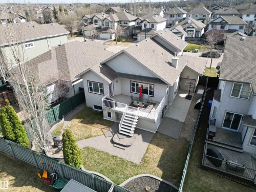 Rear exterior featuring a spacious elevated deck with white railings, stairs to a paver patio, and a fenced yard with mature plantings - 2335 Rutherford Way, Edmonton, AB - Outdoor