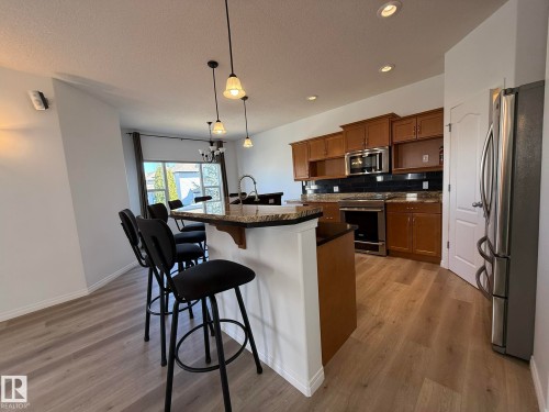Kitchen featuring wood cabinetry, stainless steel microwave, black tile backsplash, and a granite countertop breakfast bar with pendant lighting - 2335 Rutherford Way, Edmonton, AB - Indoor Photo Showing Kitchen