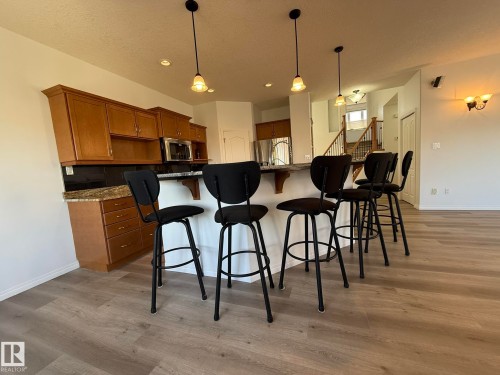 Kitchen island featuring a stainless steel dishwasher, light wood cabinetry with brushed nickel hardware, and a dark stone countertop with a matching backsplash - 2335 Rutherford Way, Edmonton, AB - Indoor Photo Showing Kitchen