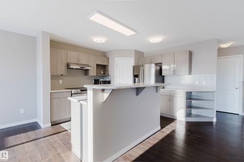 Open-concept kitchen featuring an island with a breakfast bar, stainless steel appliances, light wood-finish cabinetry, white subway tile backsplash, and dark wood-finish flooring - 16627 18 Avenue, Edmonton, AB - Indoor Photo Showing Kitchen With Upgraded Kitchen