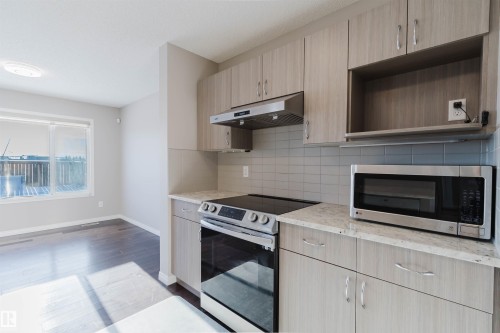 Modern kitchen featuring light wood-finish cabinetry, light-toned countertops, subway tile backsplash, stainless steel appliances, and wood-finish flooring - 16627 18 Avenue, Edmonton, AB - Indoor Photo Showing Kitchen
