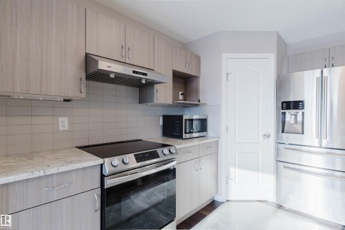 Modern kitchen featuring light wood-finish cabinetry, stainless steel appliances, a white tile backsplash, and light-toned countertops - 16627 18 Avenue, Edmonton, AB - Indoor Photo Showing Kitchen With Upgraded Kitchen