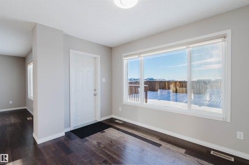Expansive window offering exterior views, dark wood-finish flooring, light neutral wall paint, white trim, and a white paneled door - 16627 18 Avenue, Edmonton, AB - Indoor Photo Showing Other Room