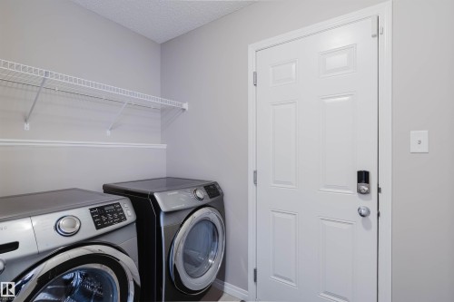 Dedicated laundry area featuring a paneled door with digital lock, overhead wire shelving, and light gray wall paint - 16627 18 Avenue, Edmonton, AB - Indoor Photo Showing Laundry Room