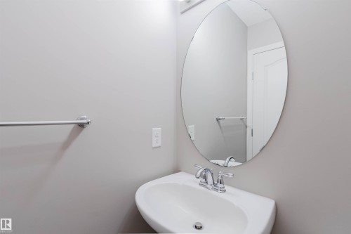 Pedestal sink featuring a chrome faucet, oval mirror, and wall-mounted towel bar - 16627 18 Avenue, Edmonton, AB - Indoor Photo Showing Bathroom
