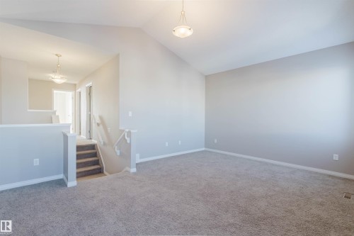 Vaulted ceiling great room with neutral carpet flooring, recessed lighting, and a prominent banister featuring a carpeted staircase - 16627 18 Avenue, Edmonton, AB - Indoor Photo Showing Other Room