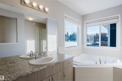 Spacious bathroom featuring a built-in corner bathtub, dual windows, a double vanity with stone-finish countertop, and integrated sinks with chrome faucets - 16627 18 Avenue, Edmonton, AB - Indoor Photo Showing Bathroom