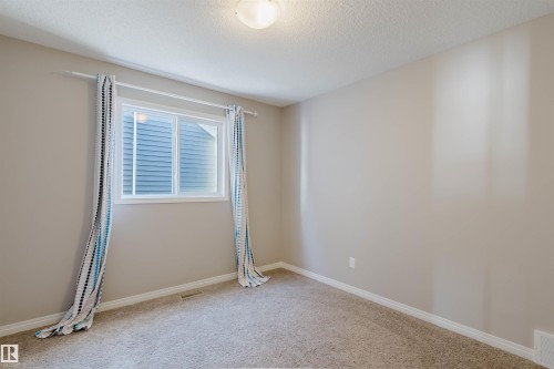 Bright room featuring a window with white trim, light neutral wall paint, white baseboards, and textured carpeting - 16627 18 Avenue, Edmonton, AB - Indoor Photo Showing Other Room