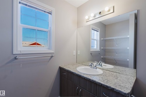 Bathroom vanity featuring a speckled countertop, undermount sink with chrome fixtures, and wood-finish cabinetry - 16627 18 Avenue, Edmonton, AB - Indoor Photo Showing Bathroom
