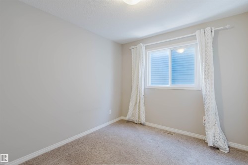 Carpeted room featuring a window with white blinds, a ceiling-mounted light fixture, white baseboards, and neutral wall paint - 16627 18 Avenue, Edmonton, AB - Indoor