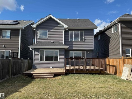 Rear exterior featuring gray horizontal siding, an upper-level window bank, a lower-level window bank, a ground-level wood deck with railing, and a small grassy area - 16627 18 Avenue, Edmonton, AB - Outdoor