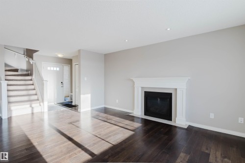 Living area featuring dark wood-finish flooring, a white mantel fireplace, recessed ceiling lighting, and a carpeted staircase leading to an upper level - 16627 18 Avenue, Edmonton, AB - Indoor Photo Showing Living Room With Fireplace