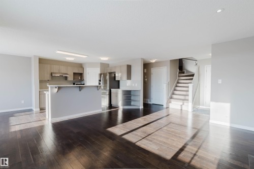 Spacious open-concept area featuring rich wood-finish flooring, a kitchen with light wood-finish cabinetry, stainless steel appliances, and a breakfast bar - 16627 18 Avenue, Edmonton, AB - Indoor Photo Showing Kitchen