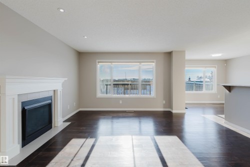Open-concept living space featuring wood-finish flooring, a white mantel fireplace with tile surround, recessed lighting, and multiple windows - 16627 18 Avenue, Edmonton, AB - Indoor Photo Showing Living Room With Fireplace